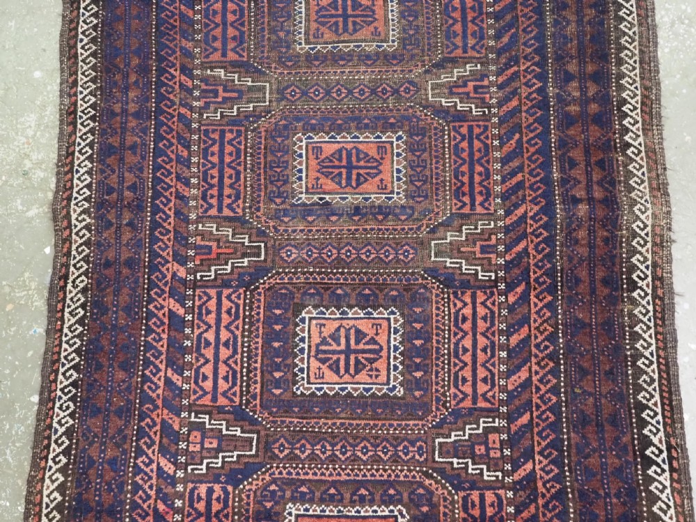 An antique rectangular Baluch tribal rug featuring five central geometric box medallions in dark red and indigo blue against a patterned ground. View IV