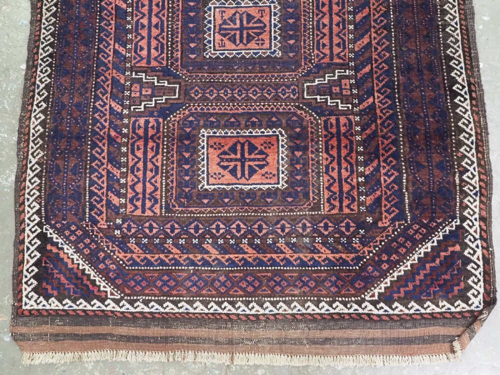 An antique rectangular Baluch tribal rug featuring five central geometric box medallions in dark red and indigo blue against a patterned ground. View V