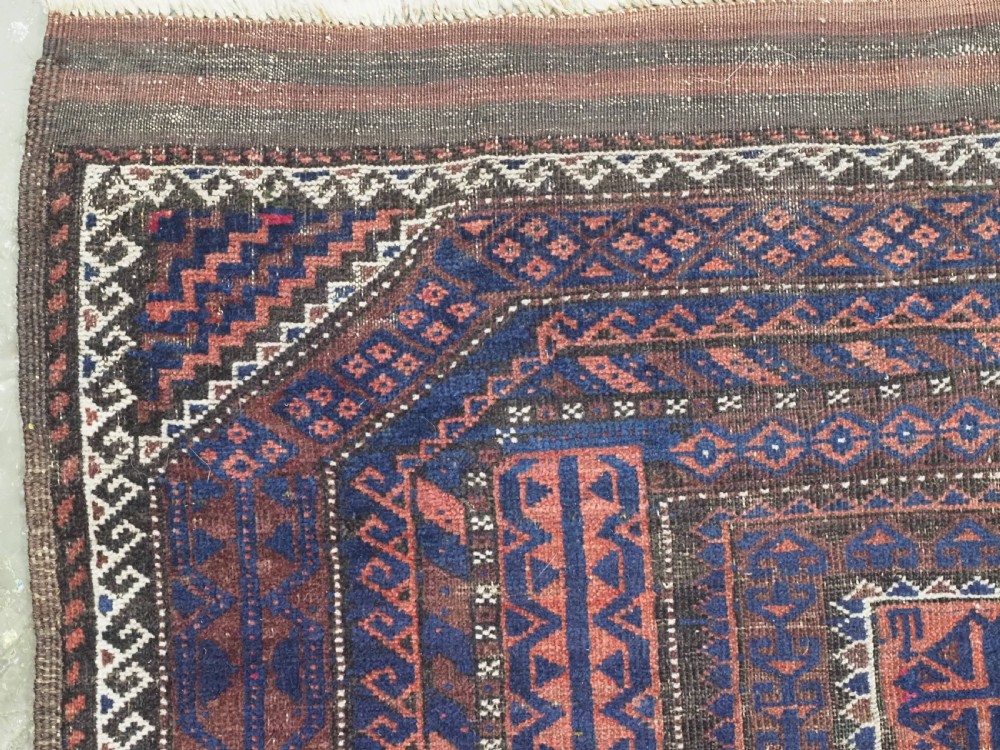 An antique rectangular Baluch tribal rug featuring five central geometric box medallions in dark red and indigo blue against a patterned ground. View VI