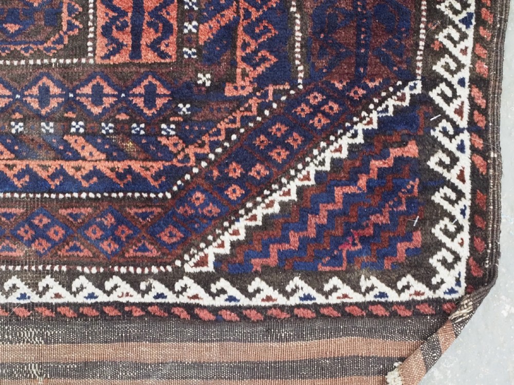 An antique rectangular Baluch tribal rug featuring five central geometric box medallions in dark red and indigo blue against a patterned ground. View X