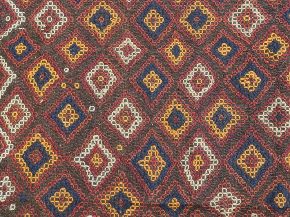 A hand-woven antique Afghan kilim textile featuring dark brown wool embroidered with a geometric diamond lattice pattern in rust, yellow, and cream, finished with long braided fringe tassels. View XI