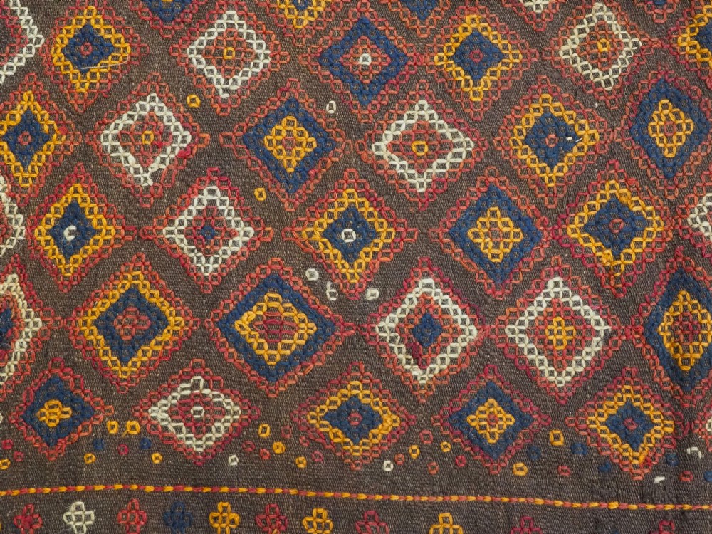 A hand-woven antique Afghan kilim textile featuring dark brown wool embroidered with a geometric diamond lattice pattern in rust, yellow, and cream, finished with long braided fringe tassels. View XII