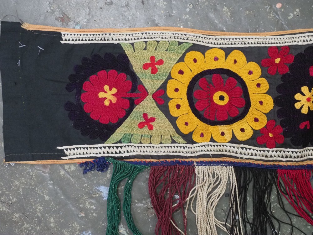 A V-shaped black cloth band decorated with vibrant red and yellow silk embroidered rosettes and finished with multi-coloured yarn fringe. View II