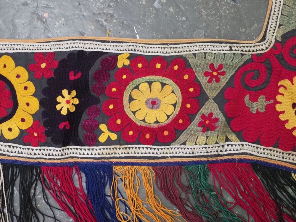 A V-shaped black cloth band decorated with vibrant red and yellow silk embroidered rosettes and finished with multi-coloured yarn fringe. View III