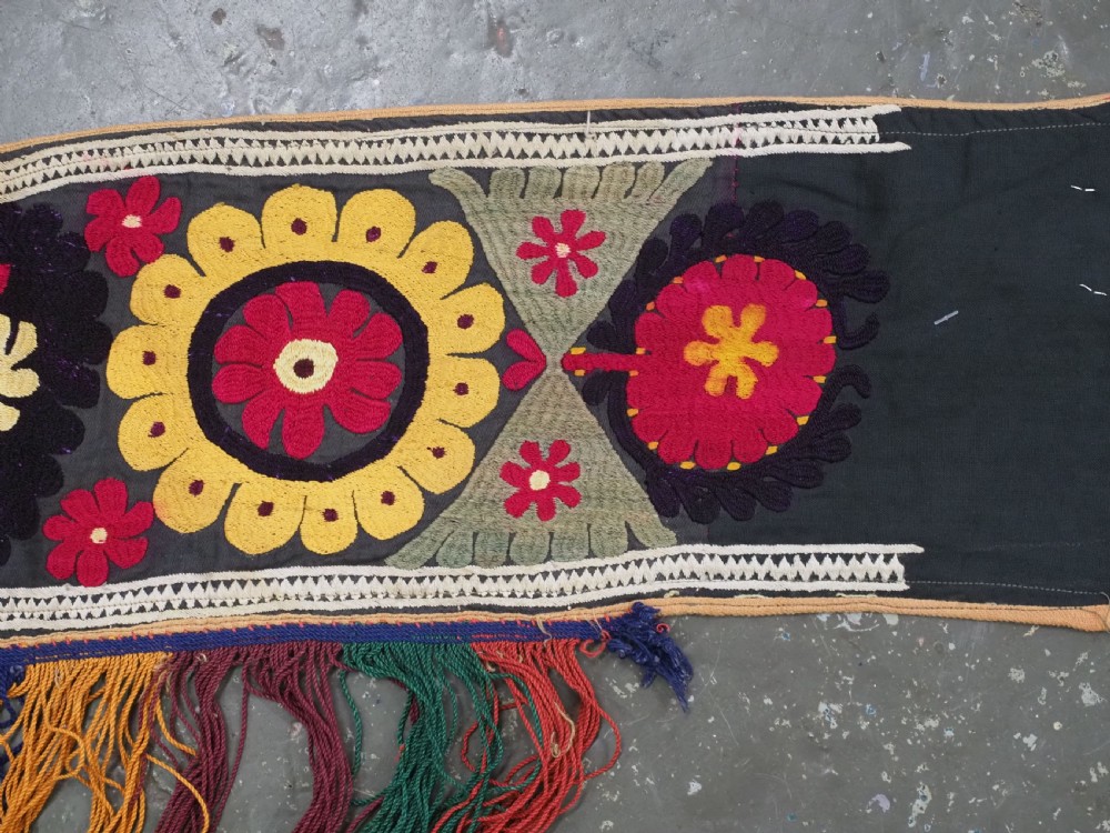 A V-shaped black cloth band decorated with vibrant red and yellow silk embroidered rosettes and finished with multi-coloured yarn fringe. View VI