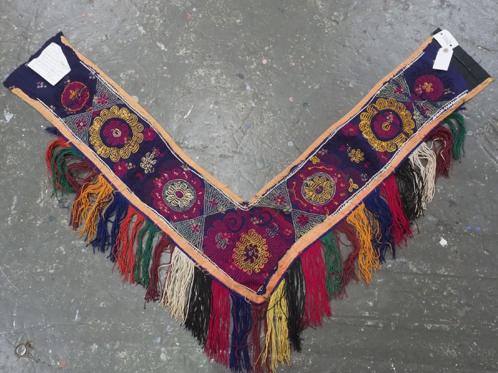 A V-shaped black cloth band decorated with vibrant red and yellow silk embroidered rosettes and finished with multi-coloured yarn fringe. View VII