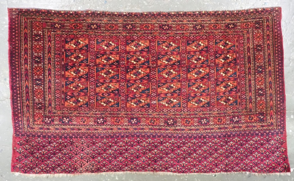 A rectangular late 19th-century Tekke Turkmen chuval face woven in madder red and navy wool featuring repeated geometric Aina gul motifs above a detailed floral elem skirt.