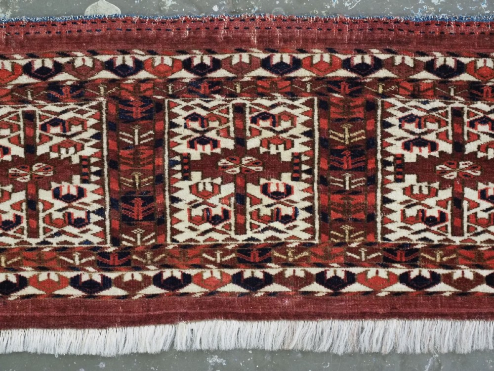 A horizontal handwoven Tekke Turkmen wool textile featuring three rectangular panels with tree designs bordered by intricate geometric patterns in red, navy, and ivory. View IV