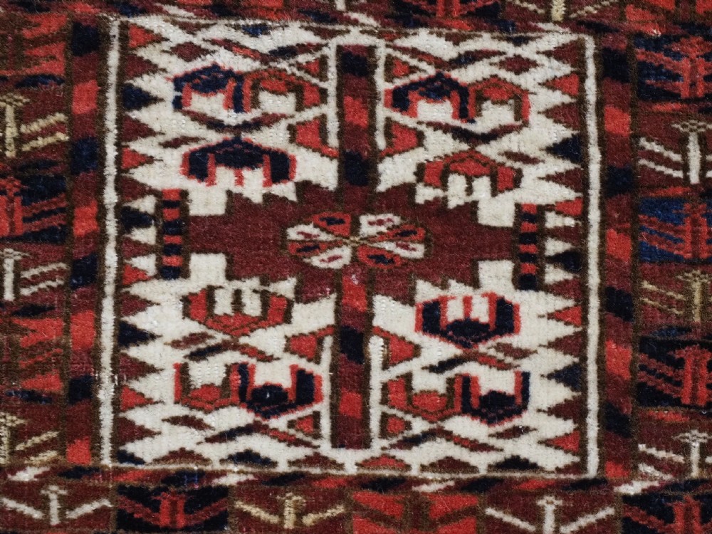 A horizontal handwoven Tekke Turkmen wool textile featuring three rectangular panels with tree designs bordered by intricate geometric patterns in red, navy, and ivory. View X