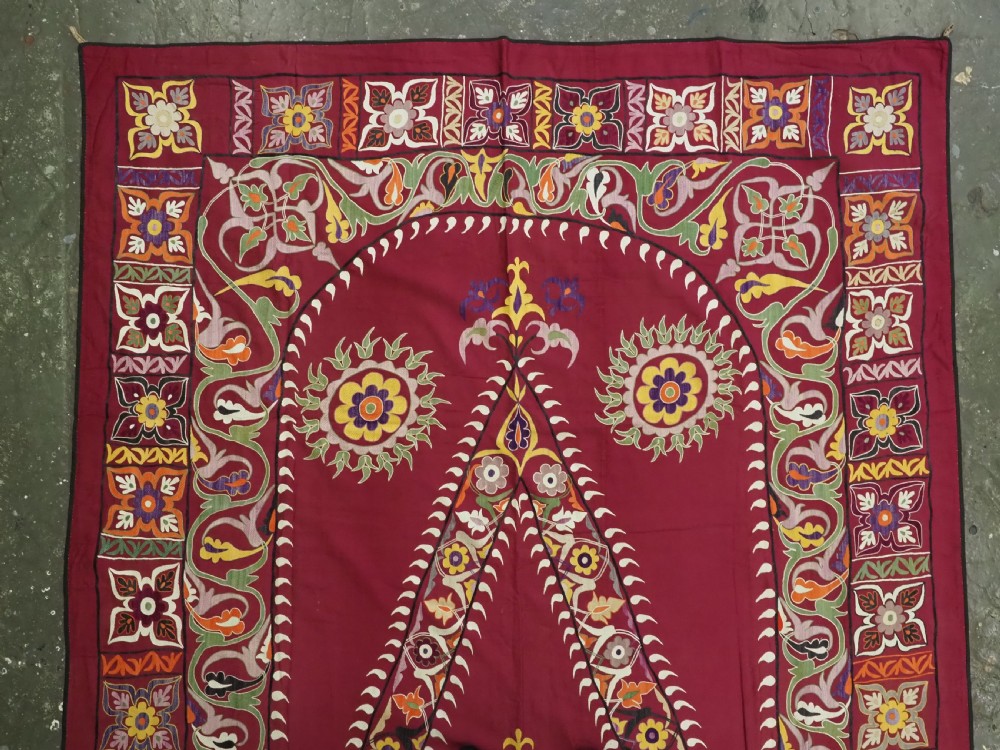 An antique rectangular Uzbek suzani featuring silk floral needlework embroidery on a deep red cotton ground with a pointed arch motif and floral borders. View II