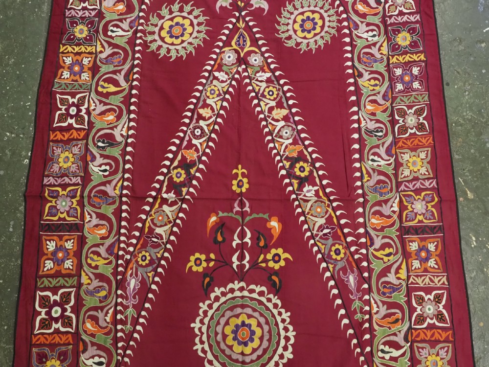 An antique rectangular Uzbek suzani featuring silk floral needlework embroidery on a deep red cotton ground with a pointed arch motif and floral borders. View III