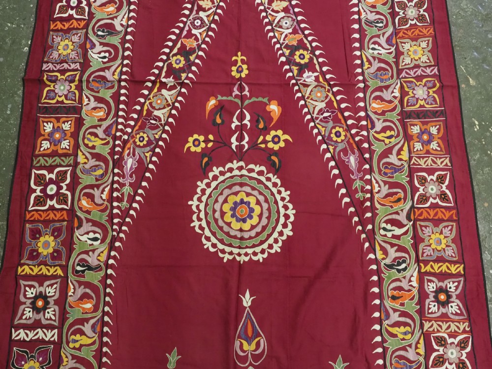 An antique rectangular Uzbek suzani featuring silk floral needlework embroidery on a deep red cotton ground with a pointed arch motif and floral borders. View IV