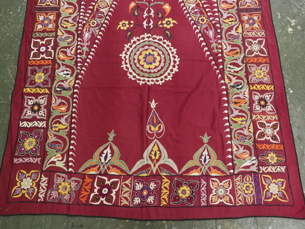 An antique rectangular Uzbek suzani featuring silk floral needlework embroidery on a deep red cotton ground with a pointed arch motif and floral borders. View V