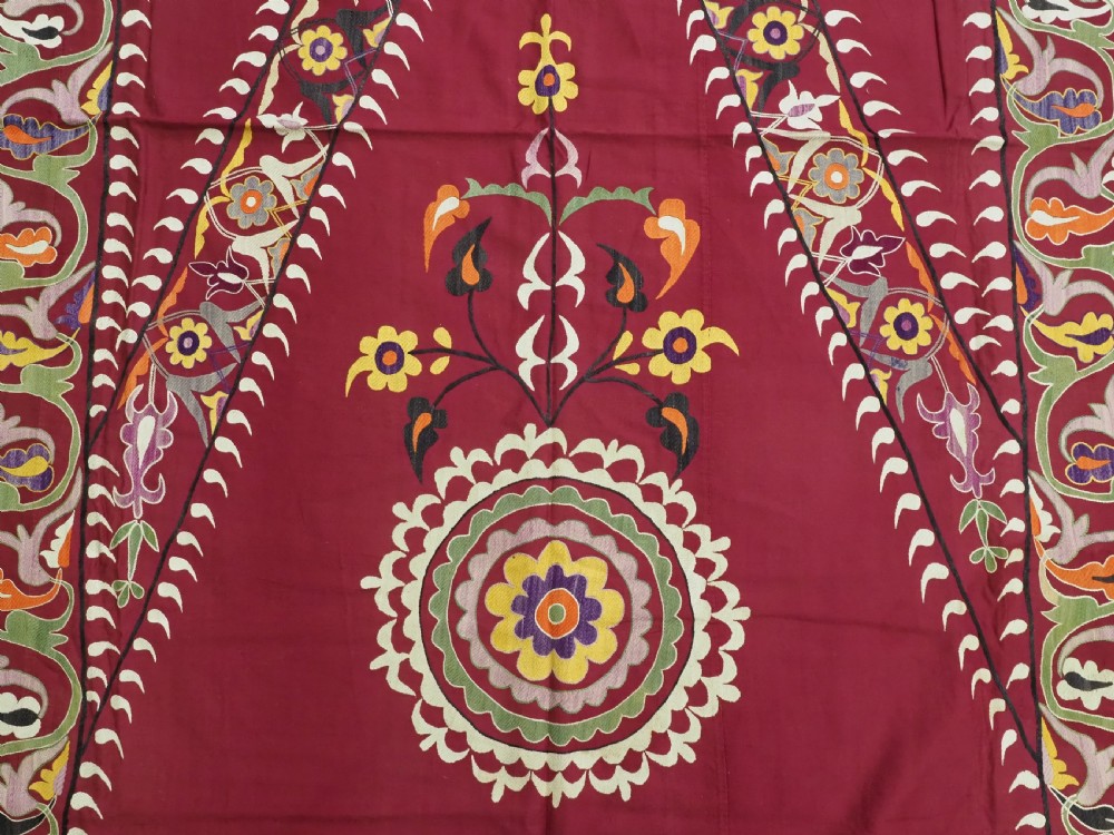An antique rectangular Uzbek suzani featuring silk floral needlework embroidery on a deep red cotton ground with a pointed arch motif and floral borders. View IX