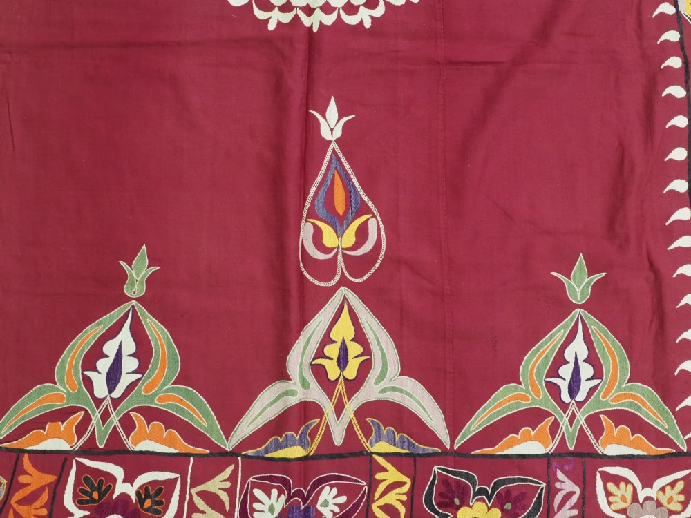 An antique rectangular Uzbek suzani featuring silk floral needlework embroidery on a deep red cotton ground with a pointed arch motif and floral borders. View XI