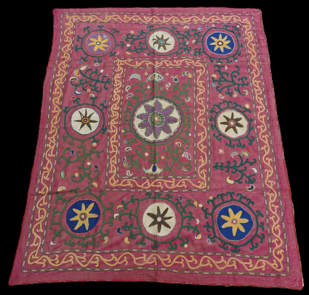 A rectangular hand-embroidered pink silk on cotton suzani textile featuring circular floral motifs, star shapes, and scrolling vine borders.