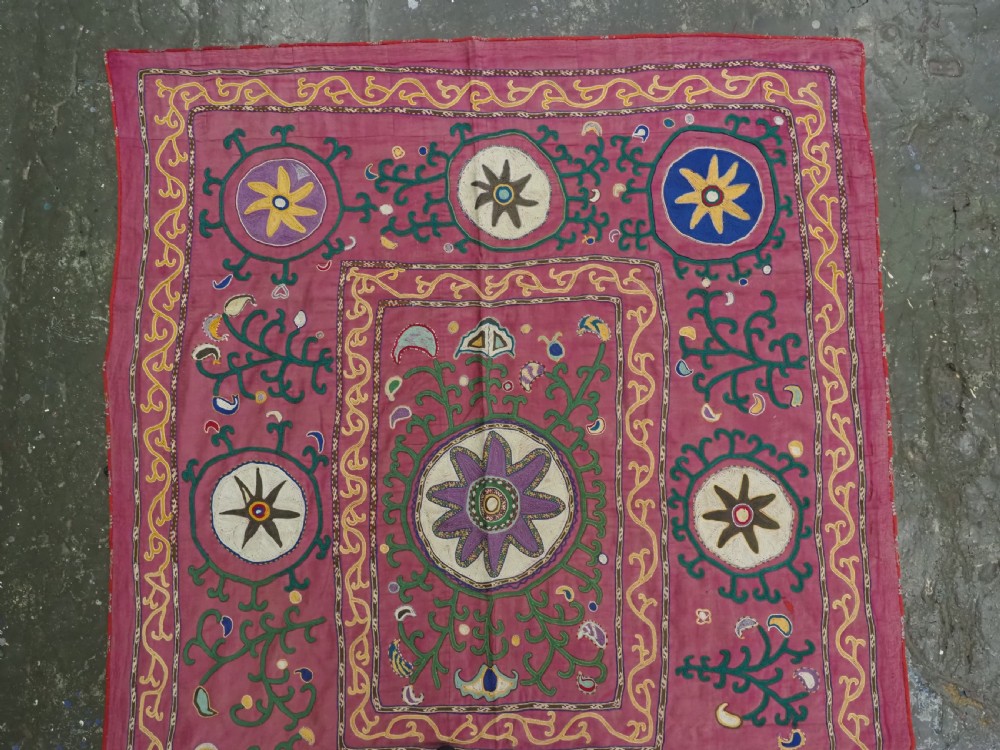 A rectangular hand-embroidered pink silk on cotton suzani textile featuring circular floral motifs, star shapes, and scrolling vine borders. View II