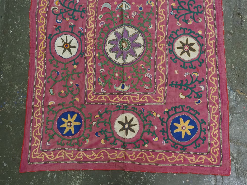 A rectangular hand-embroidered pink silk on cotton suzani textile featuring circular floral motifs, star shapes, and scrolling vine borders. View III