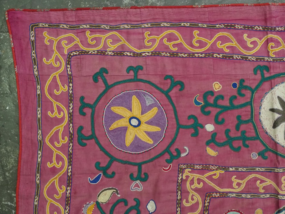 A rectangular hand-embroidered pink silk on cotton suzani textile featuring circular floral motifs, star shapes, and scrolling vine borders. View IV