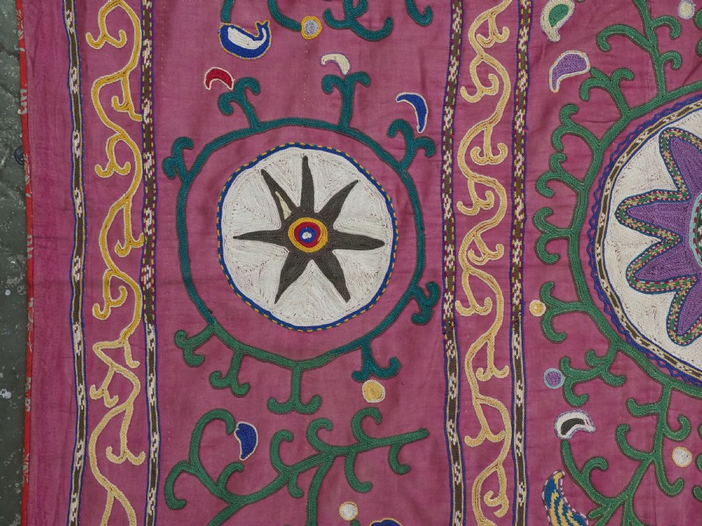 A rectangular hand-embroidered pink silk on cotton suzani textile featuring circular floral motifs, star shapes, and scrolling vine borders. View V