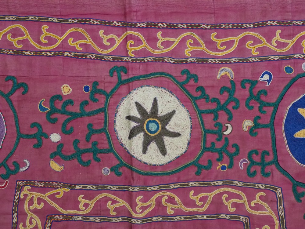 A rectangular hand-embroidered pink silk on cotton suzani textile featuring circular floral motifs, star shapes, and scrolling vine borders. View VI