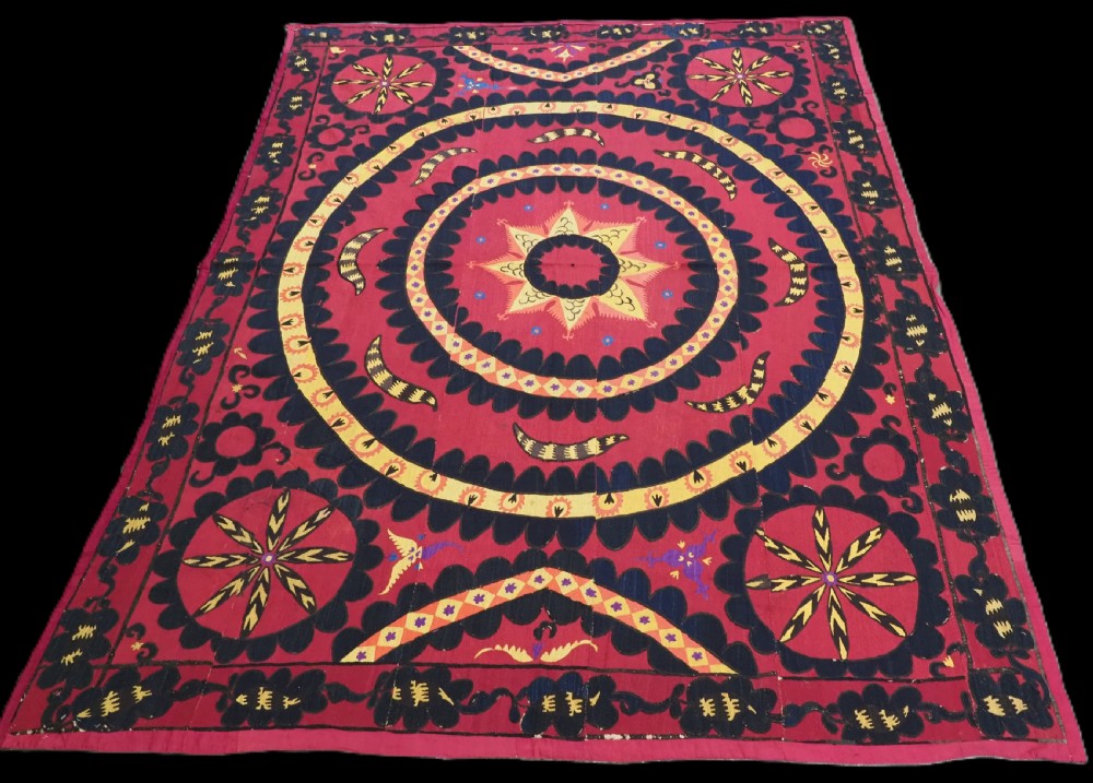 A rectangular crimson Uzbek suzani textile featuring heavy silk embroidery with a central star motif inside concentric circular borders.