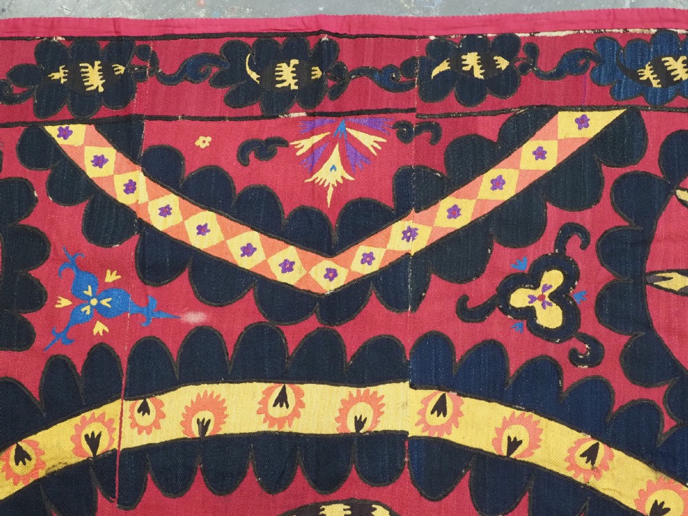 A rectangular crimson Uzbek suzani textile featuring heavy silk embroidery with a central star motif inside concentric circular borders. View VI