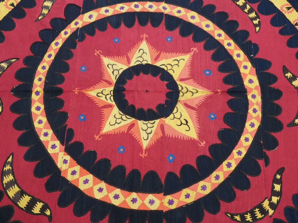 A rectangular crimson Uzbek suzani textile featuring heavy silk embroidery with a central star motif inside concentric circular borders. View VII