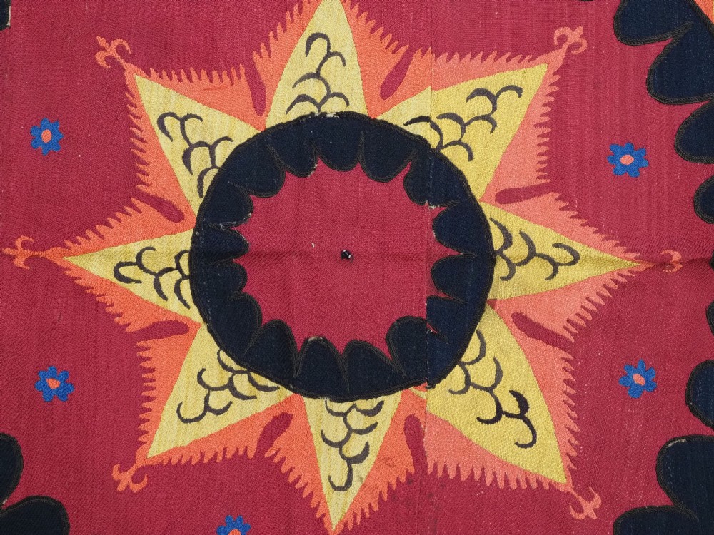 A rectangular crimson Uzbek suzani textile featuring heavy silk embroidery with a central star motif inside concentric circular borders. View VIII