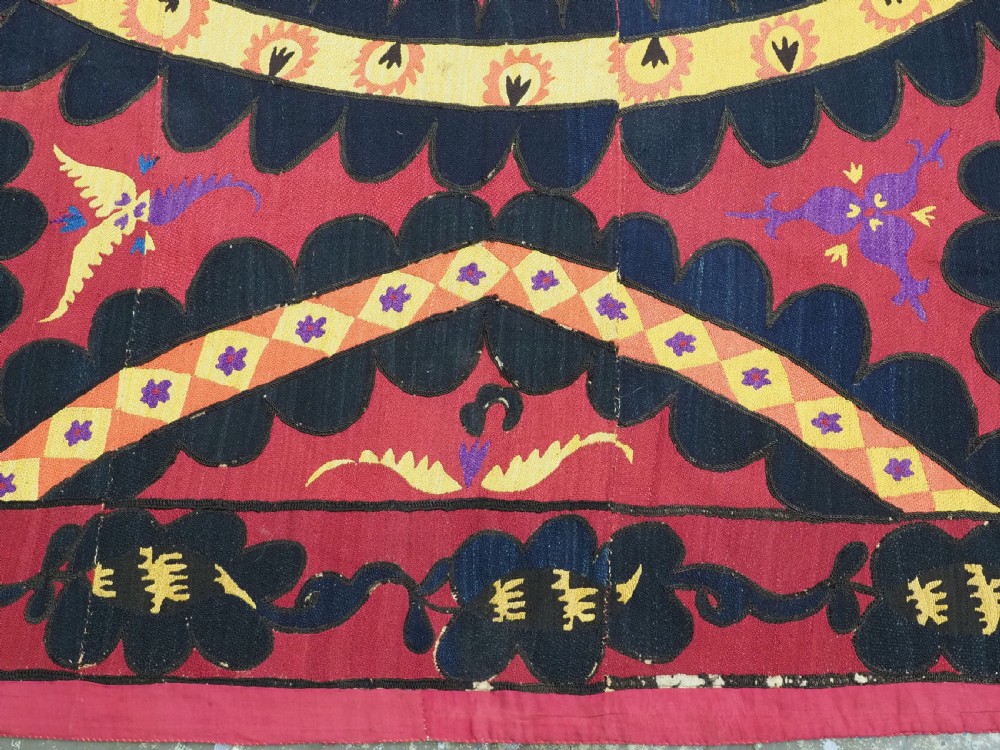 A rectangular crimson Uzbek suzani textile featuring heavy silk embroidery with a central star motif inside concentric circular borders. View IX
