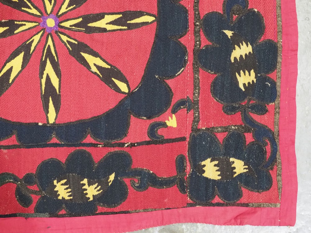 A rectangular crimson Uzbek suzani textile featuring heavy silk embroidery with a central star motif inside concentric circular borders. View XI