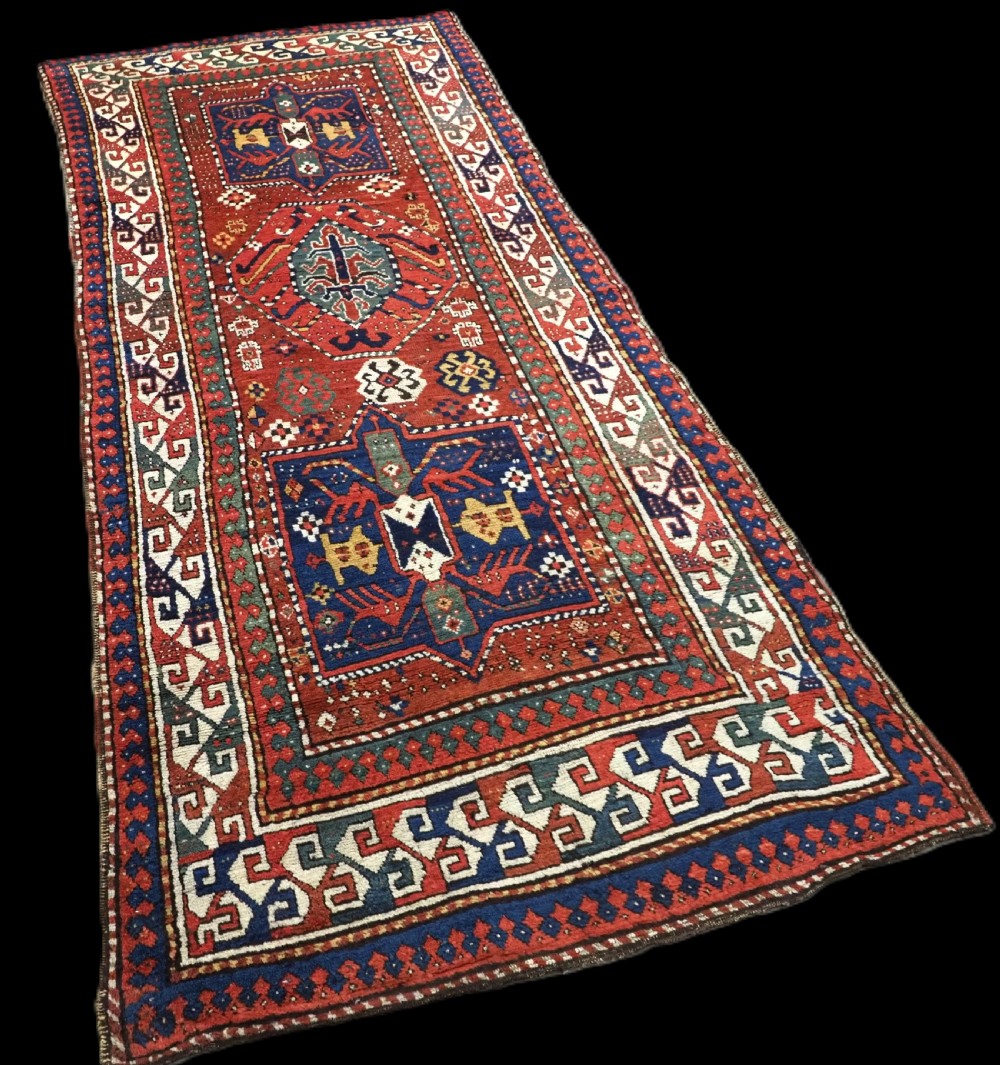 An antique Caucasian Kazak long rug featuring central geometric medallions in red, navy blue, and green with detailed border patterns. View II
