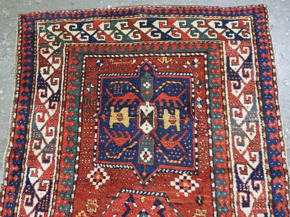 An antique Caucasian Kazak long rug featuring central geometric medallions in red, navy blue, and green with detailed border patterns. View III
