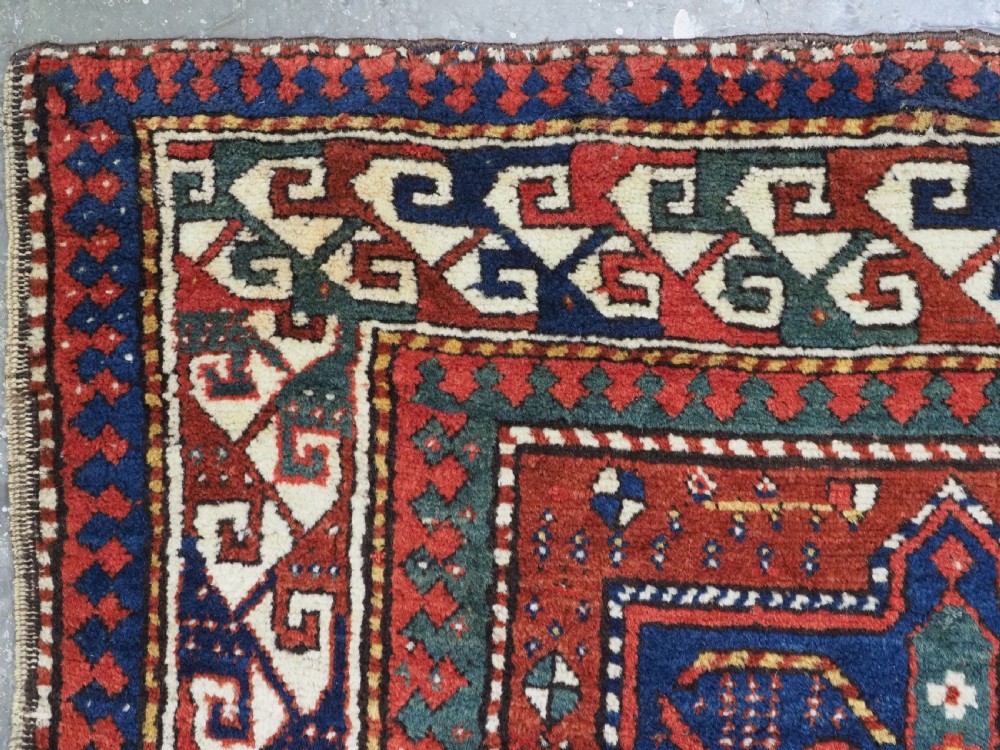An antique Caucasian Kazak long rug featuring central geometric medallions in red, navy blue, and green with detailed border patterns. View VI
