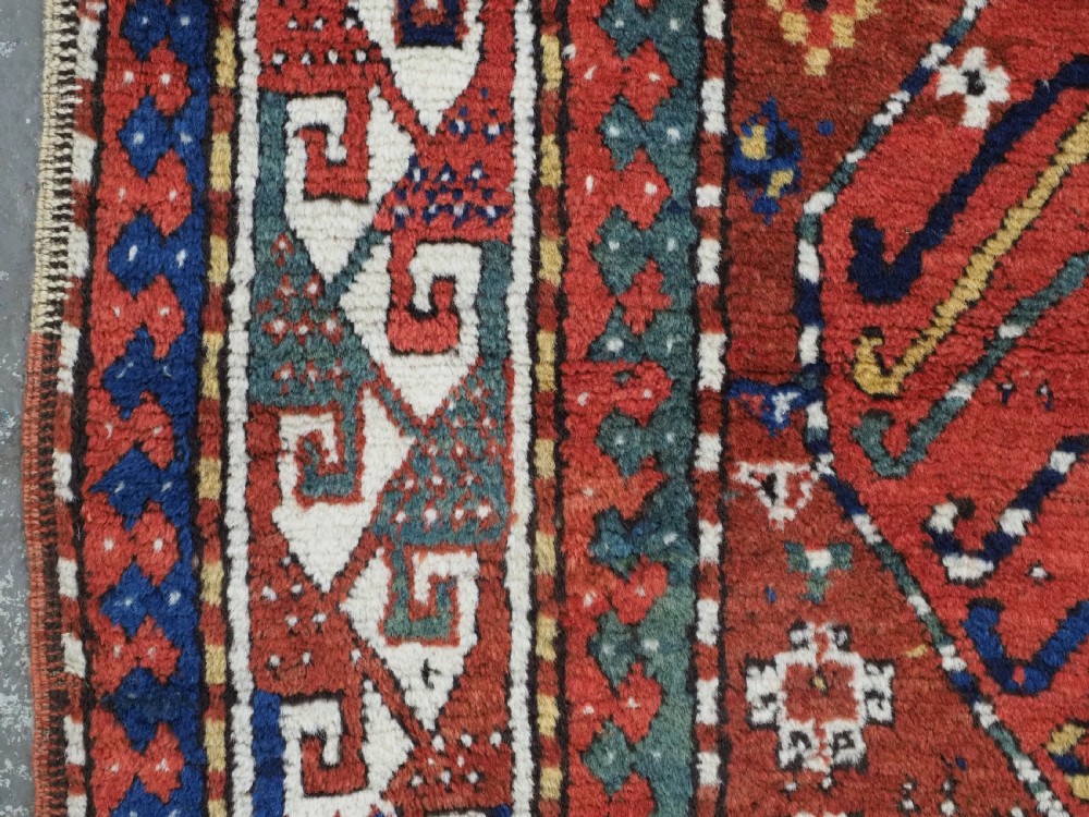 An antique Caucasian Kazak long rug featuring central geometric medallions in red, navy blue, and green with detailed border patterns. View VII