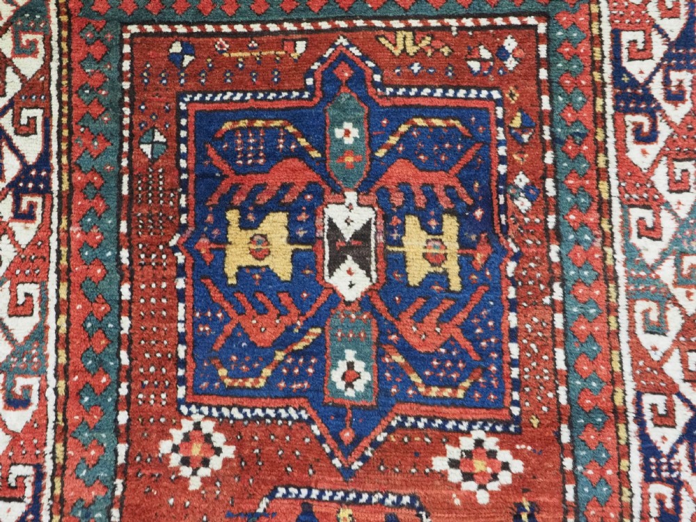 An antique Caucasian Kazak long rug featuring central geometric medallions in red, navy blue, and green with detailed border patterns. View VIII