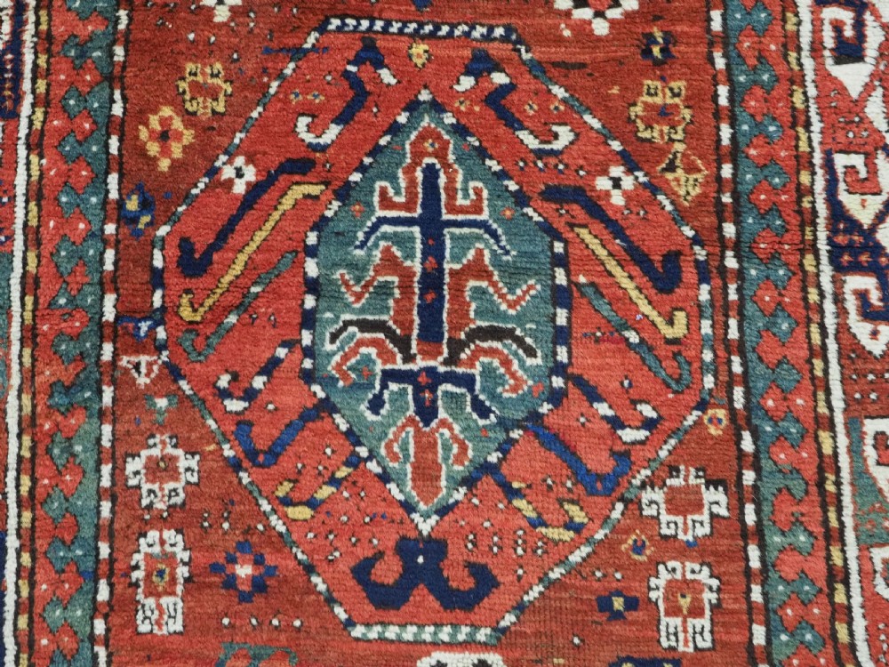 An antique Caucasian Kazak long rug featuring central geometric medallions in red, navy blue, and green with detailed border patterns. View IX