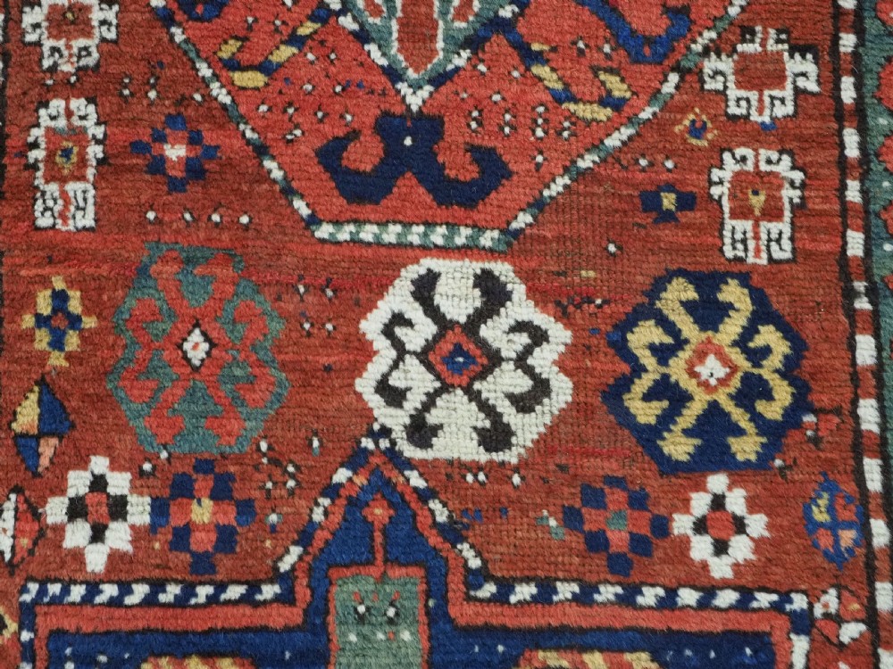 An antique Caucasian Kazak long rug featuring central geometric medallions in red, navy blue, and green with detailed border patterns. View XI