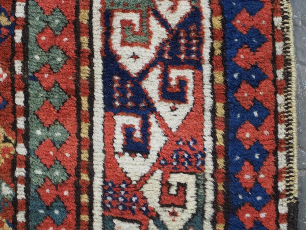 An antique Caucasian Kazak long rug featuring central geometric medallions in red, navy blue, and green with detailed border patterns. View XIII