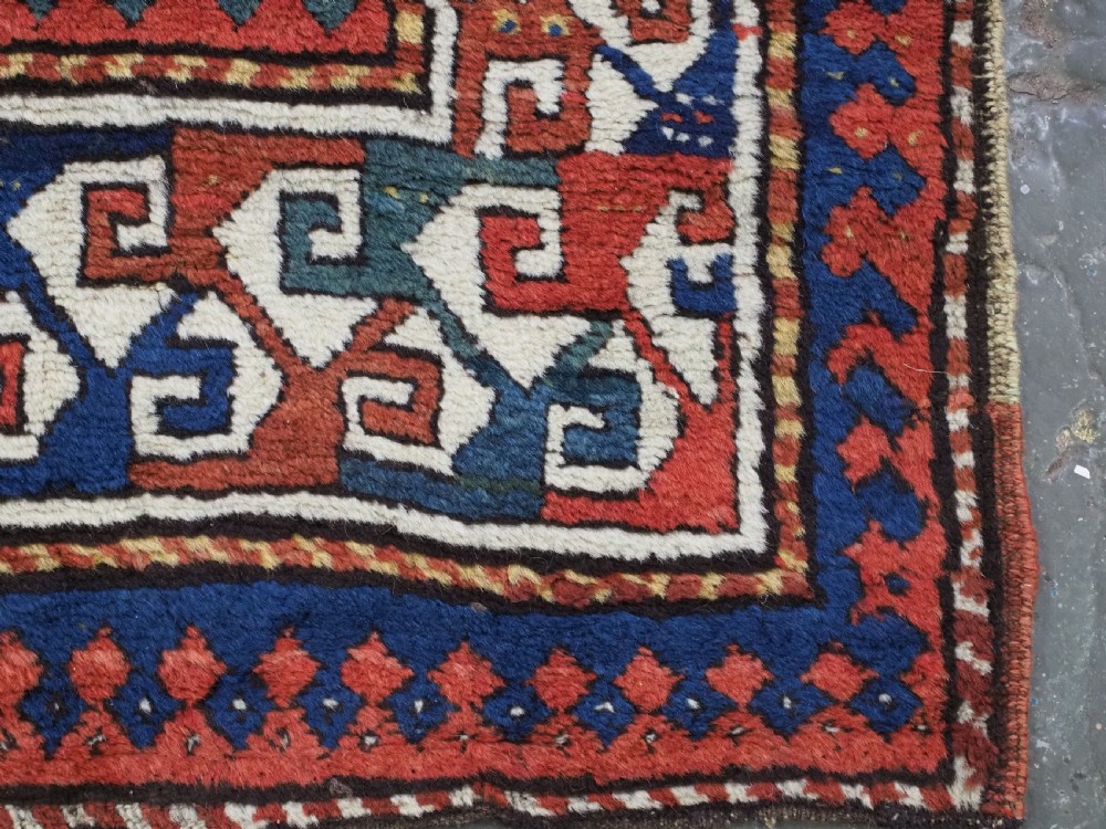 An antique Caucasian Kazak long rug featuring central geometric medallions in red, navy blue, and green with detailed border patterns. View XIV