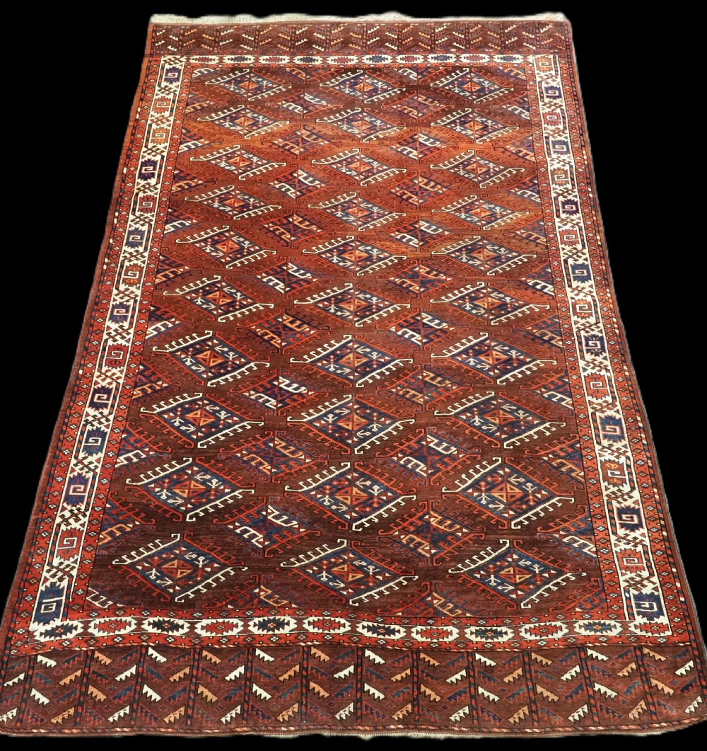 An antique Turkmen hand-knotted wool carpet featuring a repeating diamond dyrnak gul motif on a deep terracotta field with geometric borders.