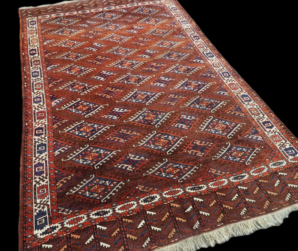 An antique Turkmen hand-knotted wool carpet featuring a repeating diamond dyrnak gul motif on a deep terracotta field with geometric borders. View II