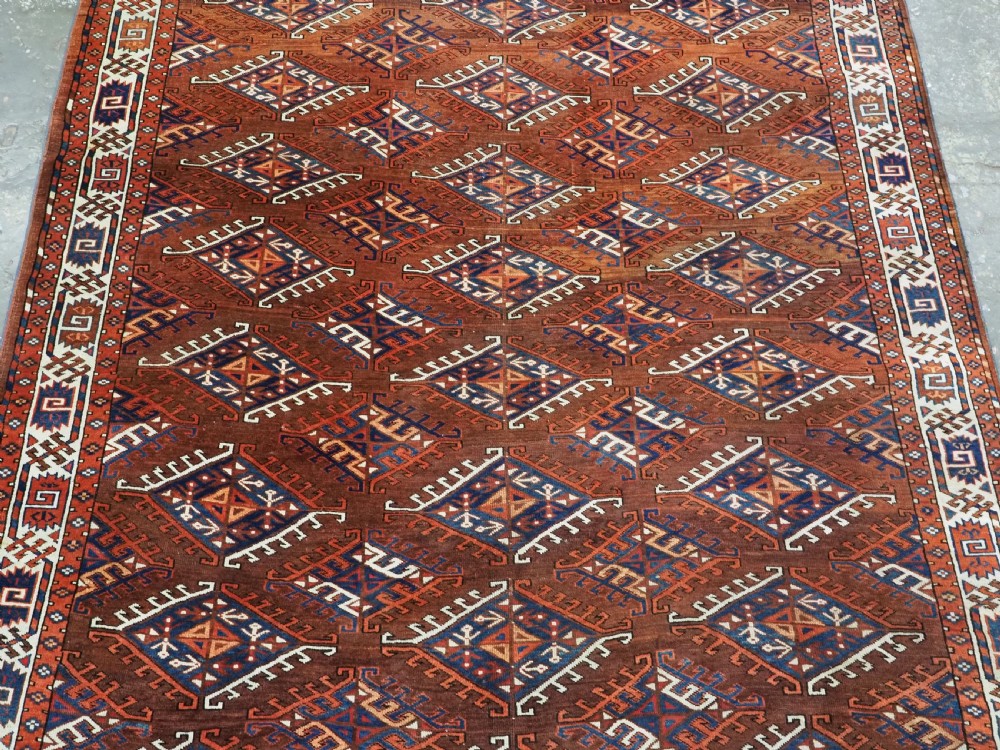 An antique Turkmen hand-knotted wool carpet featuring a repeating diamond dyrnak gul motif on a deep terracotta field with geometric borders. View IV