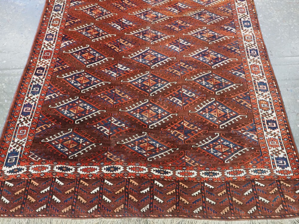 An antique Turkmen hand-knotted wool carpet featuring a repeating diamond dyrnak gul motif on a deep terracotta field with geometric borders. View V