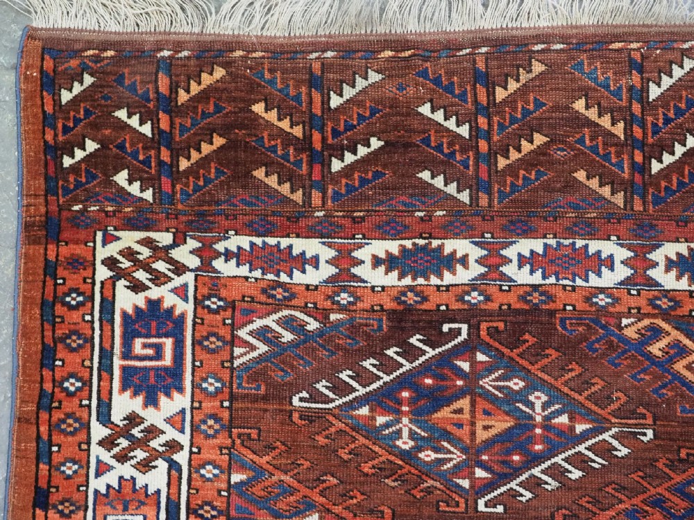 An antique Turkmen hand-knotted wool carpet featuring a repeating diamond dyrnak gul motif on a deep terracotta field with geometric borders. View VI