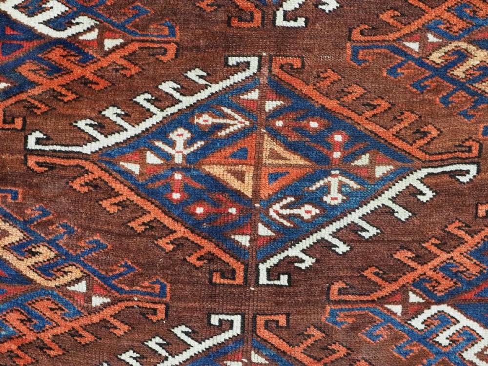 An antique Turkmen hand-knotted wool carpet featuring a repeating diamond dyrnak gul motif on a deep terracotta field with geometric borders. View X