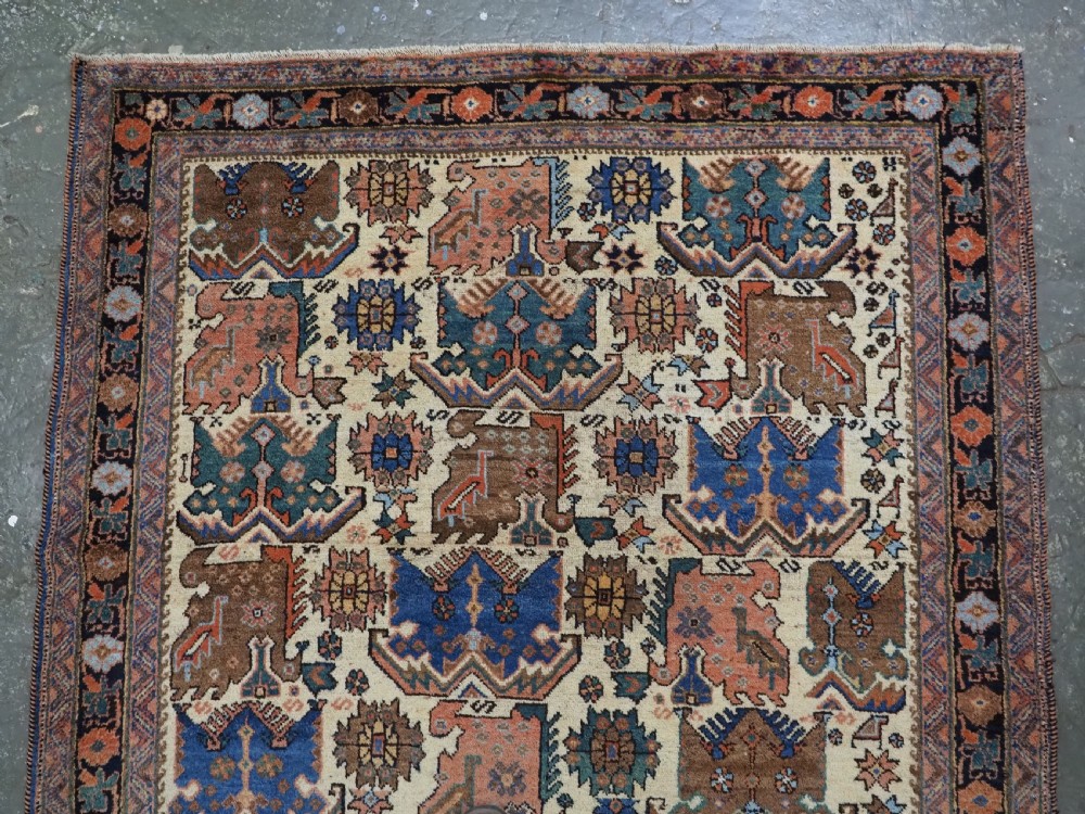 An antique hand-knotted Afshar wool rug featuring stylised dragon and phoenix motifs in blue, terracotta, and brown over an ivory ground within a geometric patterned border. View III