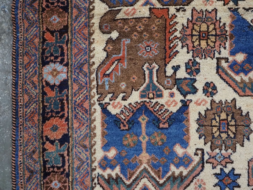 An antique hand-knotted Afshar wool rug featuring stylised dragon and phoenix motifs in blue, terracotta, and brown over an ivory ground within a geometric patterned border. View VI