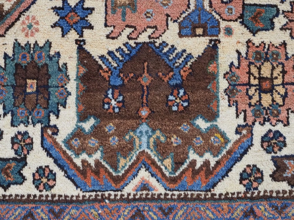An antique hand-knotted Afshar wool rug featuring stylised dragon and phoenix motifs in blue, terracotta, and brown over an ivory ground within a geometric patterned border. View X