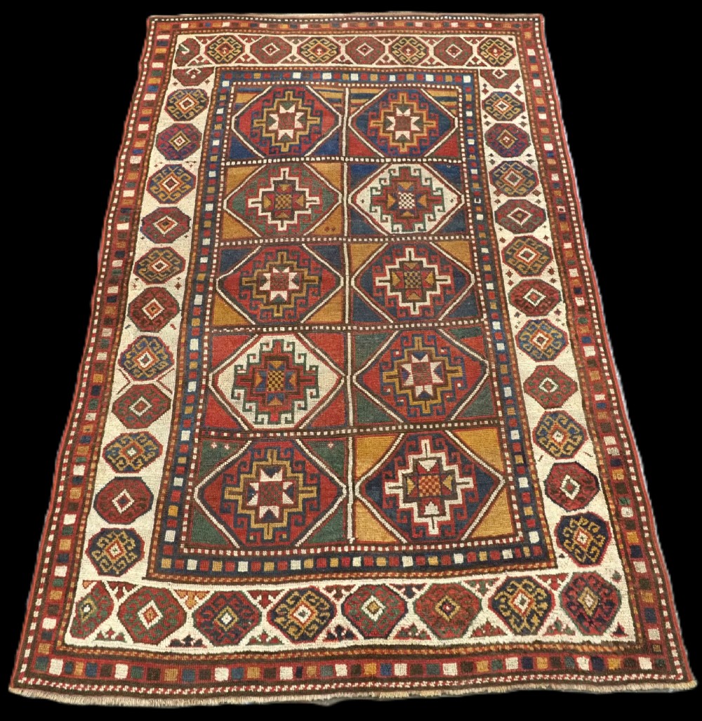 An antique hand-knotted Caucasian Moghan Kazak wool rug featuring a grid of geometric latch-hook medallions framed by patterned borders.